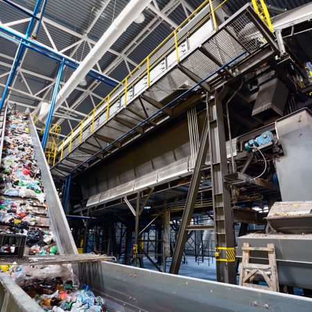 Wide angle view at recycling plant conveyor belt transports garbage inside drum filter or rotating cylindrical sieve with trommel for sorting pieces of garbage into various sizes fractions.